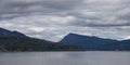 Treed Island with Homes and ferry passing by, surrounded by ocean and mountains. Royalty Free Stock Photo