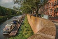 Trees, aquatic vegetation and boats anchored in pier on the bank of the river Dommel and blue sky in s-Hertogenbosch. Royalty Free Stock Photo