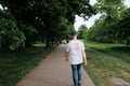 A man in jeans and a light t-shirt walks along a paved path through a lush green park. Greenwich, UK. Royalty Free Stock Photo