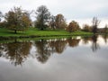 Trees with autumn leaves reflected in a lake, Ripley, North Yorkshire, UK