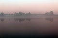 Magnificent summer nature on a pond in July. Trees, field and pond in the rays of the setting sun.