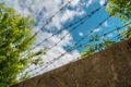 Trees peek out from behind a concrete fence with barbed wire against a beautiful sky