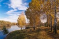 Trees with yellow leaves on the hillside by the river against a blue sky on a sunny day. Autumn landscape Royalty Free Stock Photo