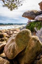 Two men sitting under a boulder are enjoying the view over the bay at low tide in Brittany, France