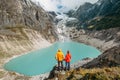 Trekkers couple dressed bright jwaterproof ackets stan on rock enjoying glacier falling in high altitude Sabai Tso glacial lake