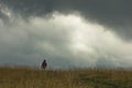 Trekking through prairie hillside under dark clouds
