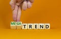 Trend or megatrend symbol. Businessman turns wooden cubes and changes words trend to megatrend. Beautiful orange table, orange
