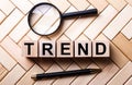 TREND word is made up of wooden cubes near a magnifying glass and a fountain pen on a wooden background. Marketing concept