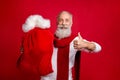 Trendy aged man plays modern santa with large velvet sack raising thumb up wear stylish sweater red background