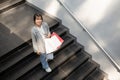 A trendy Asian woman is walking down the stairs with her shopping bags and enjoying her shopping day Royalty Free Stock Photo