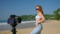 Fitness blogger records beach dance routine. Trendy attire, tropical locale, camera movements. Dance steps, upbeat