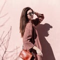 Trendy attractive young woman with beautiful long hair with sexy lips in fashionable sunglasses with bag posing standing in sun Royalty Free Stock Photo