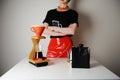 Trendy barista girl brewing filter coffee. Wood drip station. Red patent leather skirt, black t-shirt Royalty Free Stock Photo