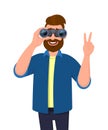 Trendy bearded man in casual wear looking through binoculars and gesturing, making victory, V, peace or number two sign with hand. Royalty Free Stock Photo