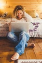 Trendy beautiful cheerful happy woman sitting on the wooden floor at home or hotel with modern laptop computer internet connected Royalty Free Stock Photo
