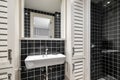 Trendy black ceramic tile bathroom creates striking contrast with white sink and light wood lockers. Mirror reflects