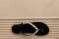 Trendy black flip flops decorated with rhinestones, standing on the beach sand. Royalty Free Stock Photo