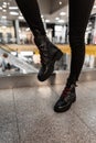 Trendy brutal leather black boots with red shoelaces on female legs. Close-up. Autumn-winter footwear. New youth fashionable