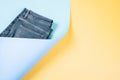 Trendy composition with part of new jeans on light blue and pastel yellow background. Abstract denim background. Denim