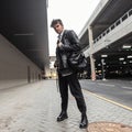 Trendy cool young man in a stylish leather black jacket in a shirt in jeans in boots with a fashion backpack with a hairstyle Royalty Free Stock Photo