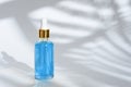 Trendy dropper glass bottle with pipette and blue liquid on white background with leaf shadow Royalty Free Stock Photo