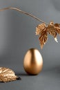 Trendy Easter background with Gold Easter egg and golden leaves on a grey color background with empty space for text. Easter Royalty Free Stock Photo