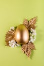 Trendy Easter background with Gold Easter egg and golden leaves on a light green color background with empty space for text. Royalty Free Stock Photo