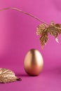 Trendy Easter background with Gold Easter egg and golden leaves on a pink color background with empty space for text. Easter Royalty Free Stock Photo