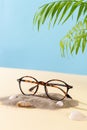 Trendy Eyeglass frame on beach with palm leaves, trendy Still Life Style. Tortoiseshell frame glasses on sand. Optic store