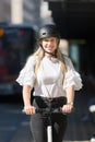 Trendy fashinable teenager, beautiful blonde girl riding public rental electric scooter in urban city environment. Eco Royalty Free Stock Photo