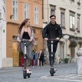 Trendy fashinable teenagers riding public rental electric scooters in urban city environment. New eco-friendly modern