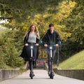 Trendy fashinable teenagers riding public rental electric scooters in urban city park. New eco-friendly modern public