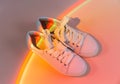 Trendy fashion white sneakers on abstract bright background. Neon lights on casual shoes. Orange and red gradient light. Royalty Free Stock Photo