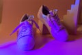 Trendy fashion white sneakers on abstract bright background. Neon lights on casual shoes. Orange and violet gradient light. M Royalty Free Stock Photo