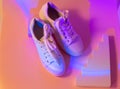 Trendy fashion white sneakers on geometry podium on abstract bright background. Neon lights on casual shoes. Violet and orange