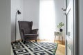 Grey wing back chair in small room with stylish black and white rug and plant in pot on small table Royalty Free Stock Photo