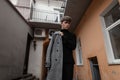 Trendy handsome young man in a fashionable plaid gray coat in black stylish sweater is standing outdoors near the vintage walls. Royalty Free Stock Photo