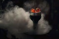 Trendy hookah bowl with red hot coals in clouds of beautiful white smoke on dark black background. Modern shisha with