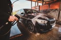 Trendy man in jeans and blaser is washing his own car at car washing station. Royalty Free Stock Photo