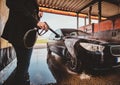 Trendy man in jeans and blaser is washing his own car at car washing station. Royalty Free Stock Photo