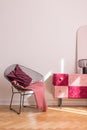 Trendy metal armchair with burgundy pillow and pink blanket next to classy suede covered cabinet, real photo with copy space on