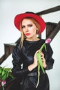 Trendy model in leather black dress and hat with flowers