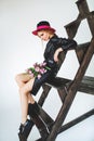 Trendy model in leather black dress and hat with flowers