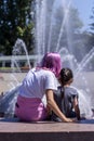 Trendy PreTeen sitting with a Young Child watching a fountain