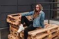 Trendy pretty young woman hipster in violet sunglasses in military hood in fashion denim jacket in jeans in white leather boots Royalty Free Stock Photo