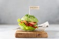 Trendy Raw Vegan avocado burger with fesh vegetables and salted salmon on wooden board on gray background. Side view. Restaurant Royalty Free Stock Photo