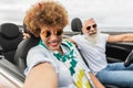 Trendy senior couple having fun taking a selfie with mobile phone in convertible car during summer vacation - Focus on mature Royalty Free Stock Photo