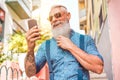 Trendy senior man using smartphone app in downtown center outdoor - Mature fashion male having fun with new trends technology -