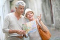 Trendy senior tourists visiting town using tablet and map