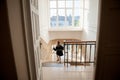 Trendy small girl in white wool hat and black coat running down stairs indoors Royalty Free Stock Photo